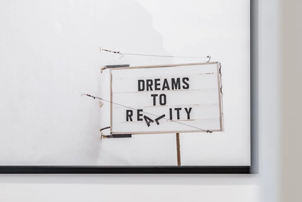 Cuadro con un cartel que dice Dreams to reality sobre una pared blanca
